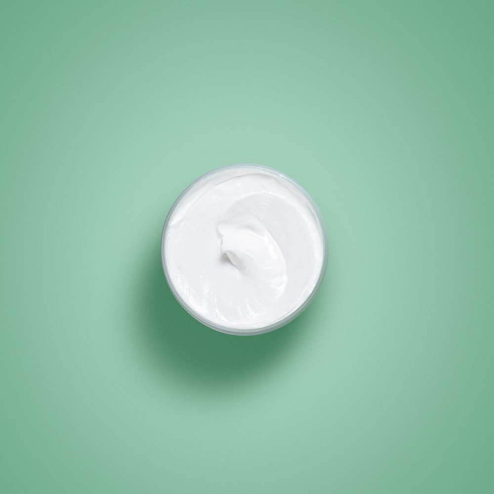 Vue de dessus de crème blanche dans un pot. Fond vert.