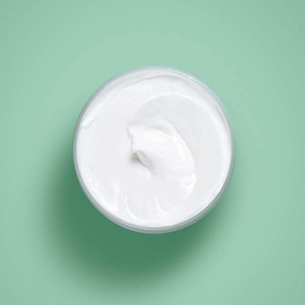 Vue de dessus d'une crème dans un pot transparent. La crème est blanche et a une texture lisse.