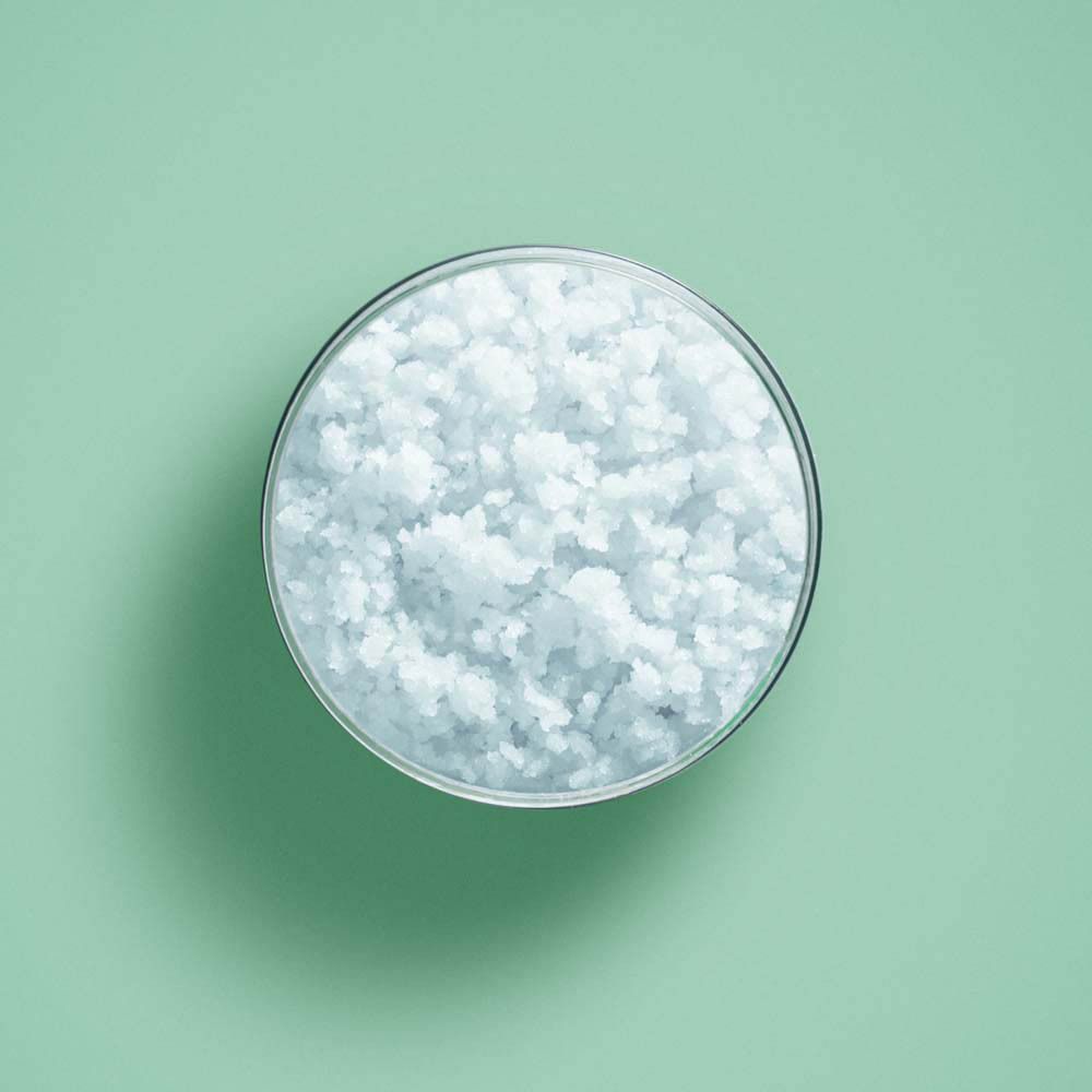 Vue de dessus d'un bol transparent avec des cristaux blancs sur fond vert.