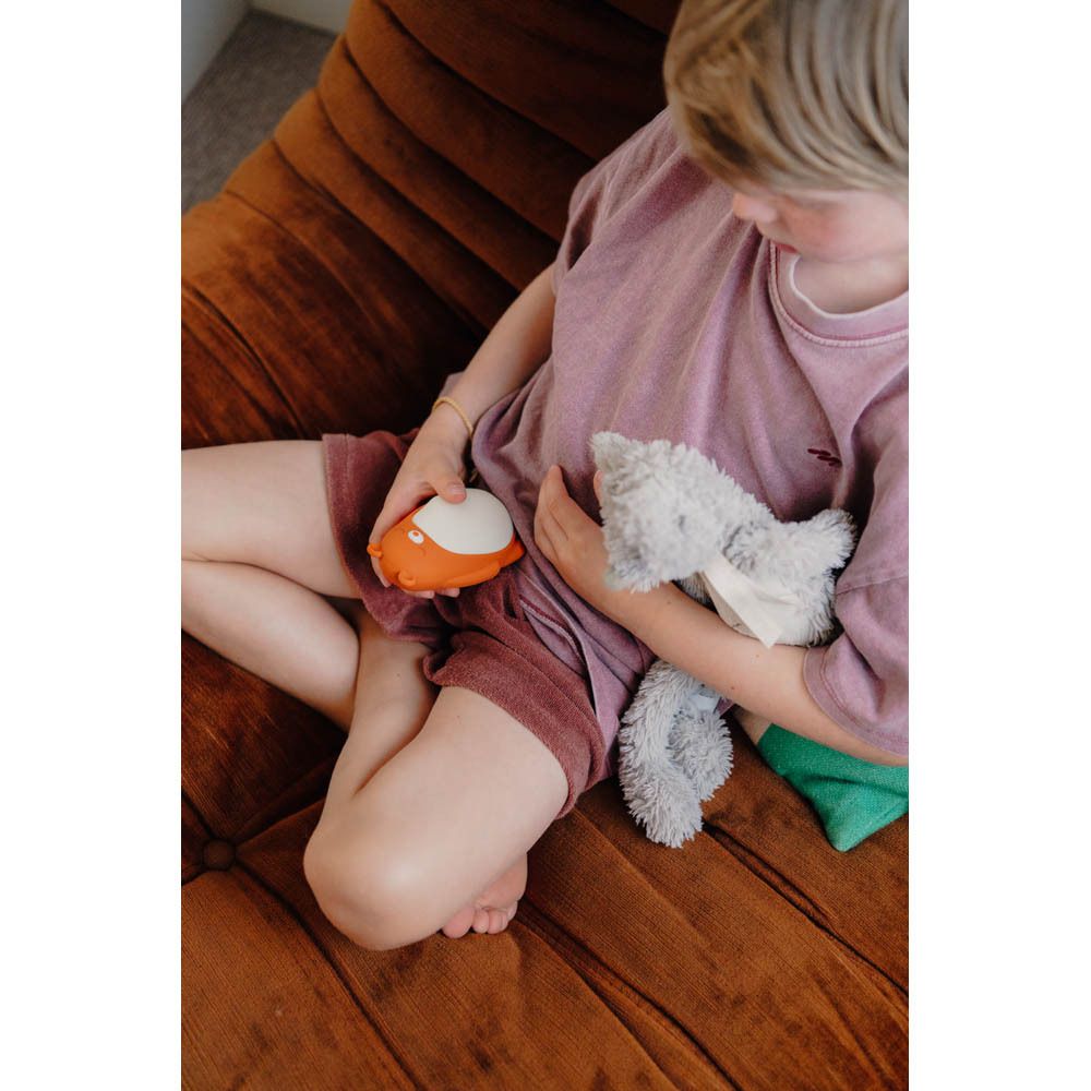 Moonbird Moonbuddy Barry l'ours, orange et blanc. Assis sur un canapé.