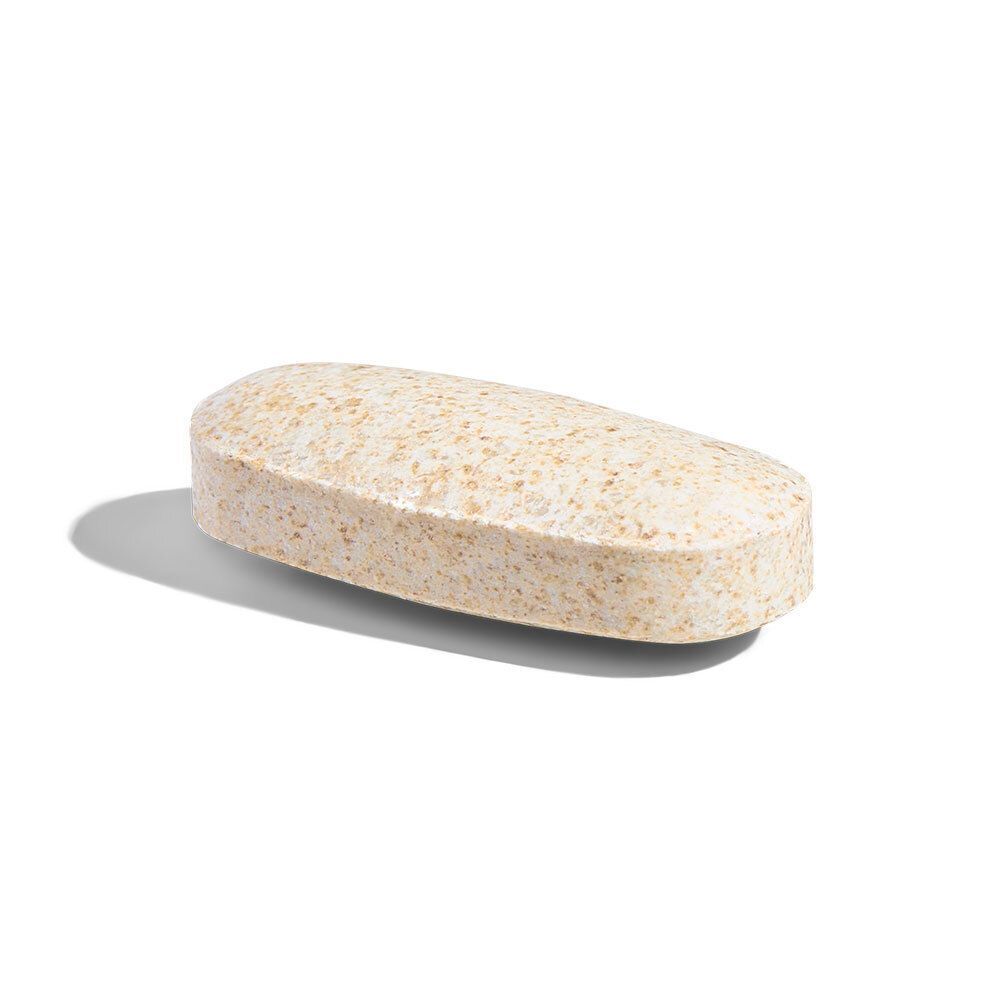 Eine einzelne Tablette. Beige, länglich, mit einer leicht strukturierten Oberfläche. Liegt auf einer weißen Oberfläche.