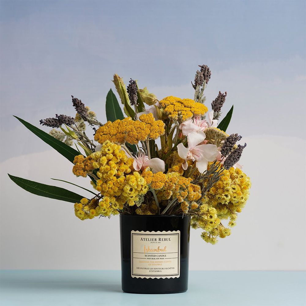 Schwarze Duftkerze im Glas, dekoriert mit einem Strauß getrockneter Blumen.