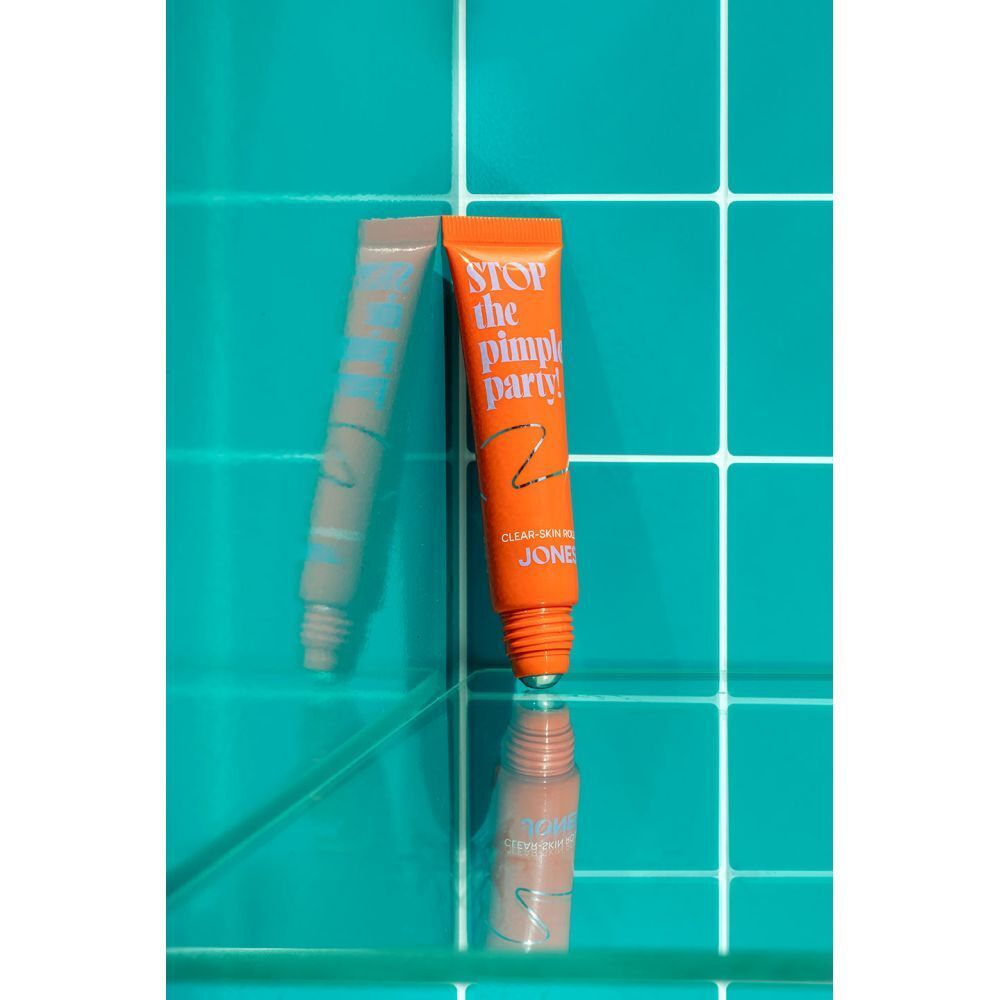 Tube orange avec texte. Texte : Stop the Pimple Party! Clear-Skin Roller. Marque : JONES. Réflexion.