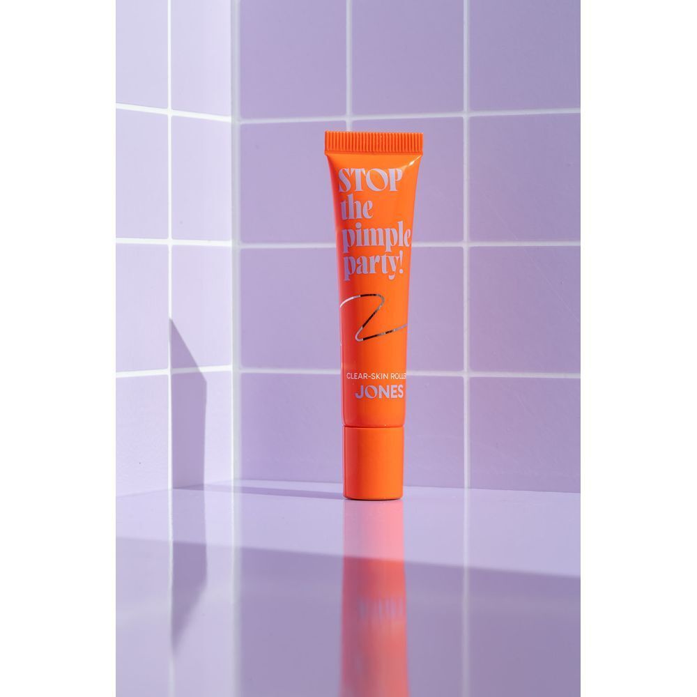 Tube orange avec texte. Texte : Stop the Pimple Party! Clear-Skin Roller. Marque : JONES. Arrière-plan.