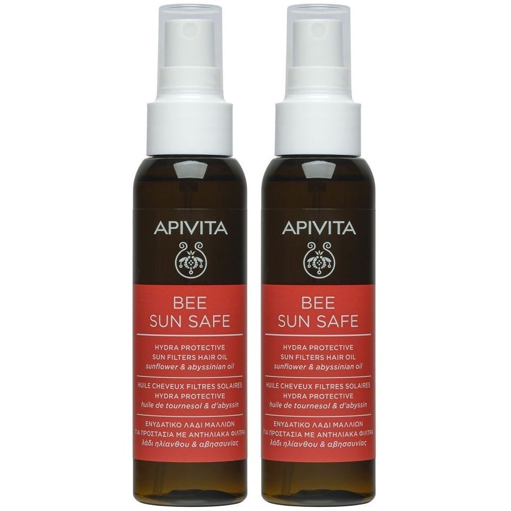 Deux flacons d'huile capillaire Apivita Bee Sun Safe. Flacons bruns avec vaporisateur blanc et étiquette rouge. Texte: Bee Sun Safe, Hydra Protective.