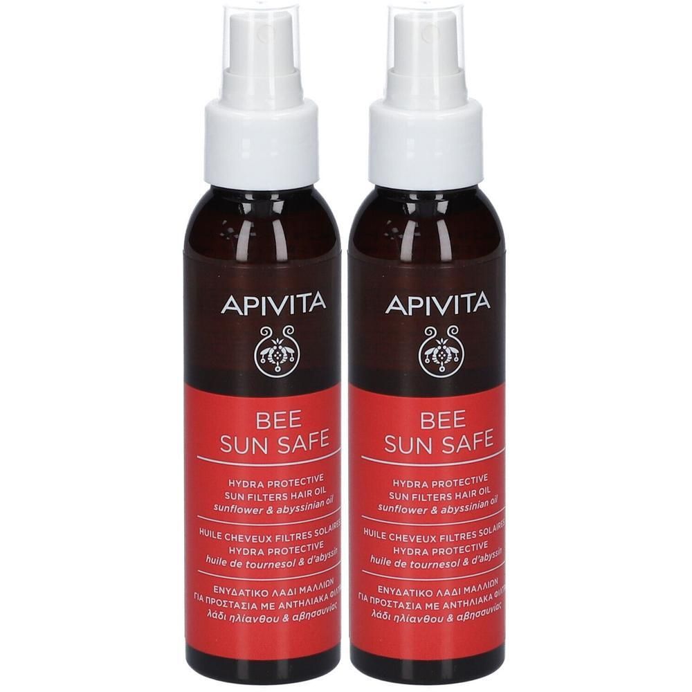 Deux flacons avec vaporisateur. Inscription: Apivita, Bee Sun Safe. Étiquette rouge avec texte. Liquide brun visible.