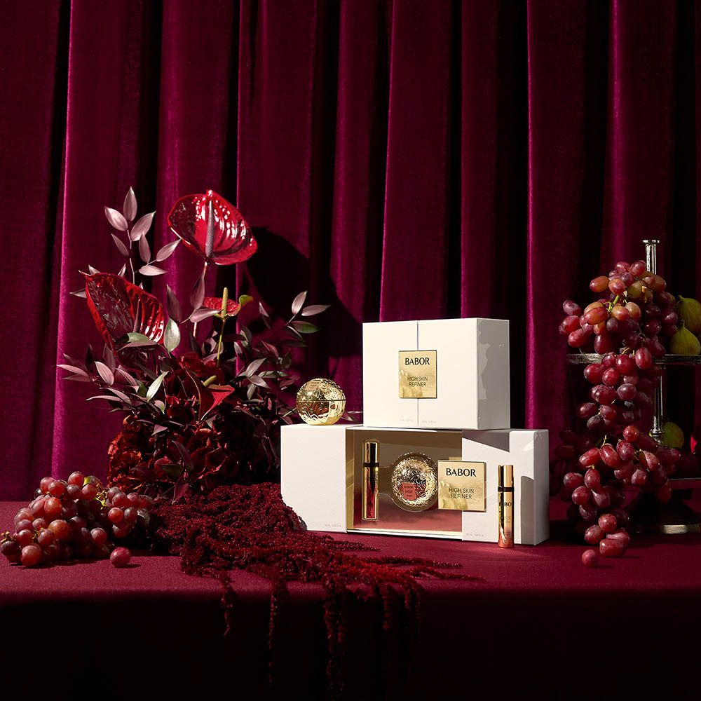 Produktpräsentation mit Geschenkboxen und Dekoration. Aufschrift: BABOR HIGH SKIN REFINER. Produkte auf rotem Tisch.