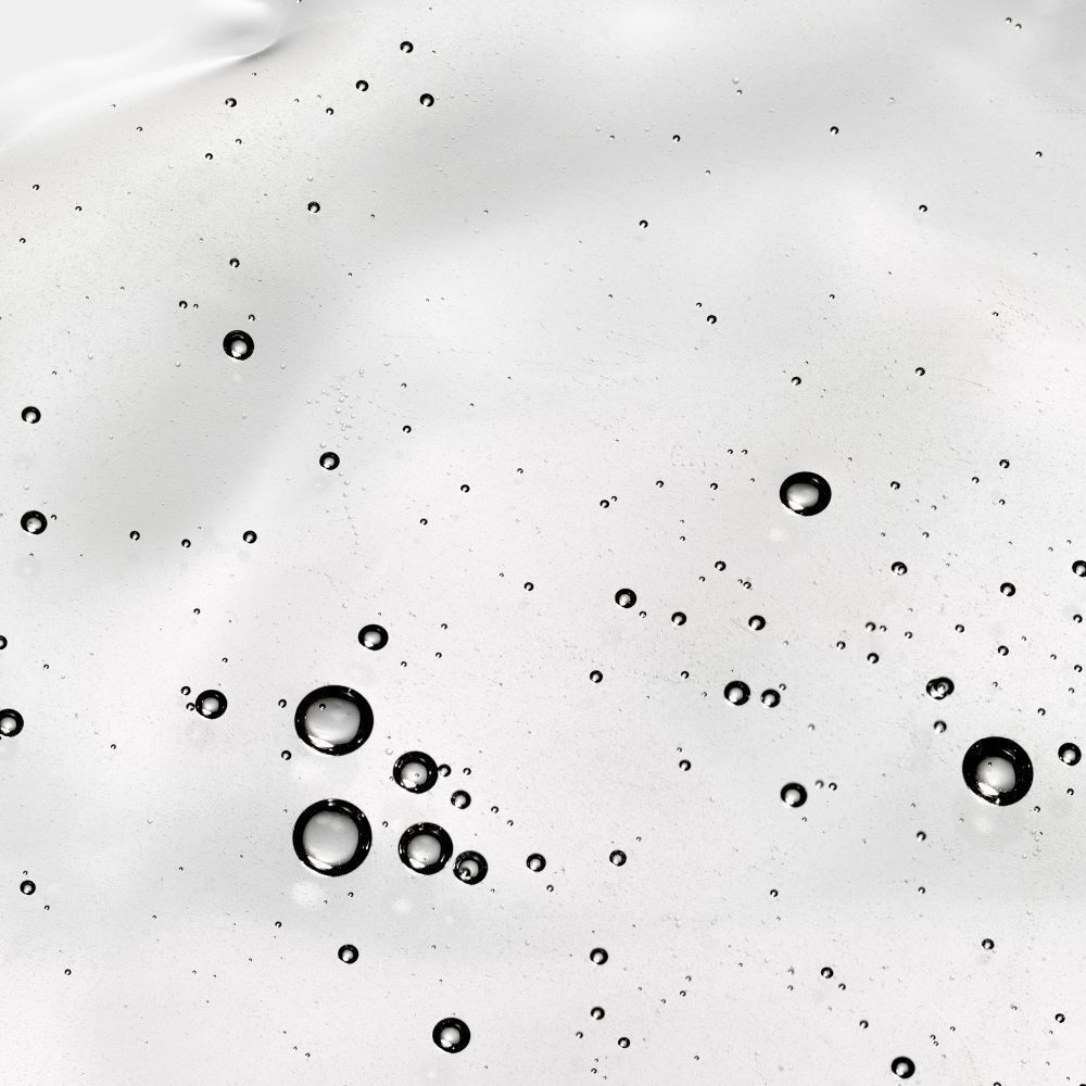 Gros plan d'un liquide clair avec de nombreuses petites bulles. Le liquide est étalé sur une surface blanche.