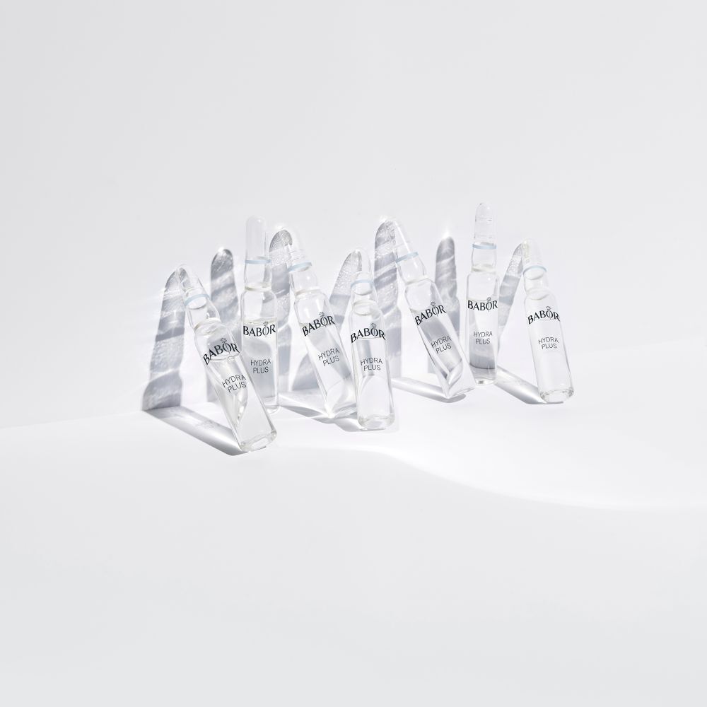 Plusieurs ampoules Babor Hydra Plus sur une surface blanche. Les ampoules projettent des ombres.