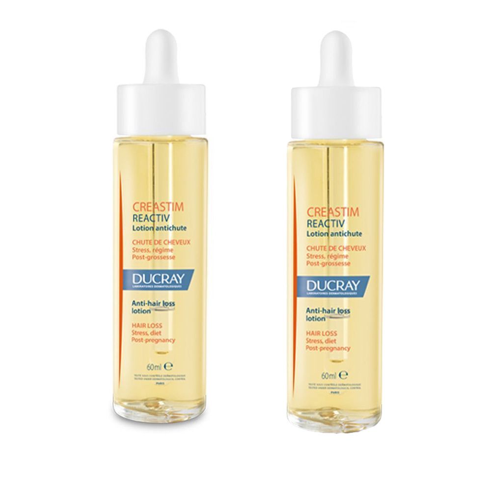 Deux flacons de lotion DUCRAY Creastim Reactiv. Liquide jaune dans des flacons en verre avec bouchon blanc et pipette. Étiquetage.