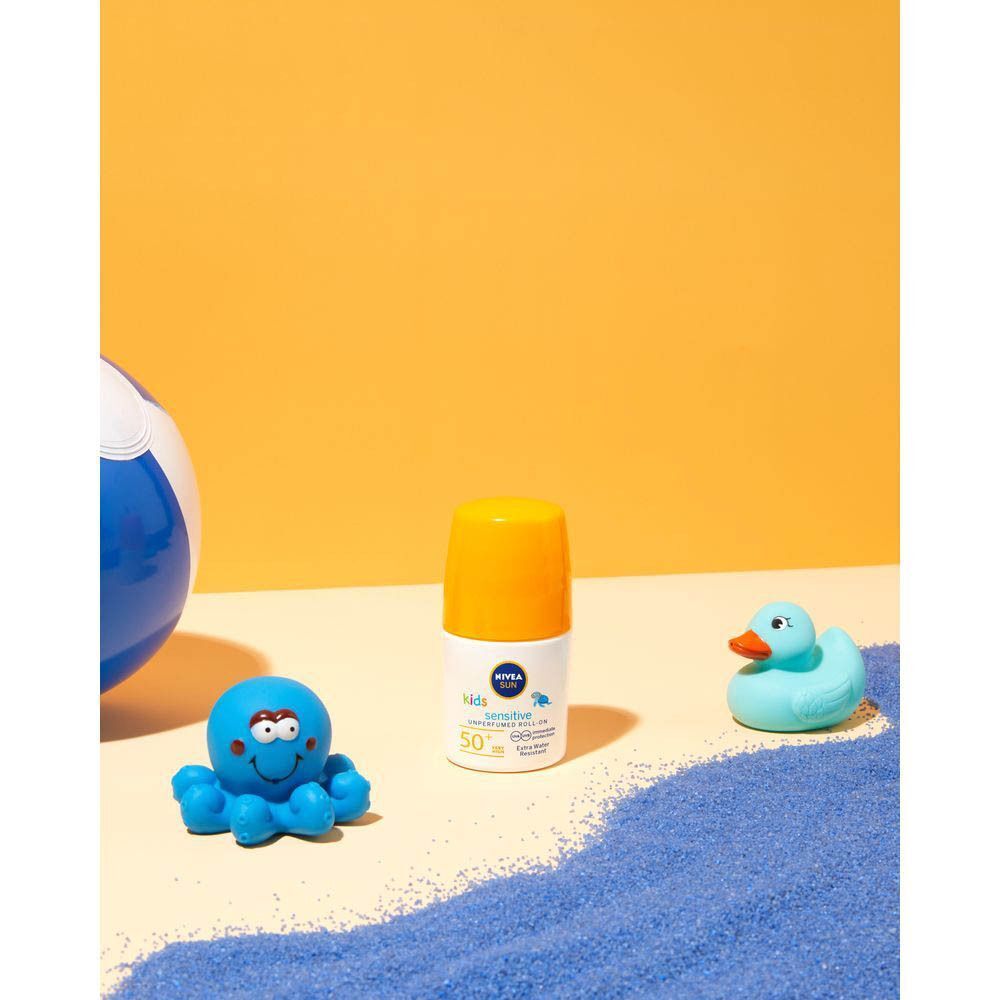 Flacon roll-on avec bouchon jaune près de jouets sur sable bleu. Inscription: NIVEA SUN babies & kids sensitive protect 50+.