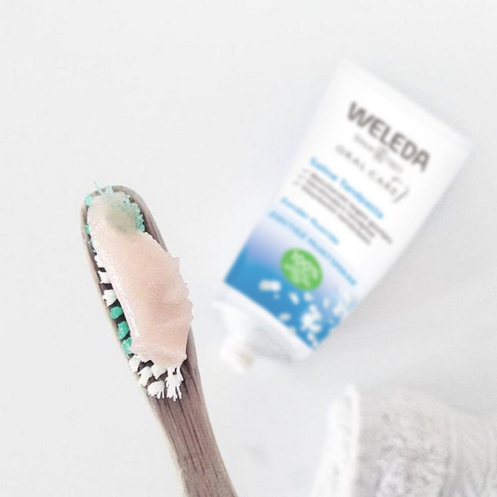 Zahnbürste mit Zahnpasta und Weleda Saline Zahnpasta Tube. Tube mit blauer und grüner Beschriftung. Text: Saline Zahnpasta, Zoutige Muntsmaak, Menthe et Sel.