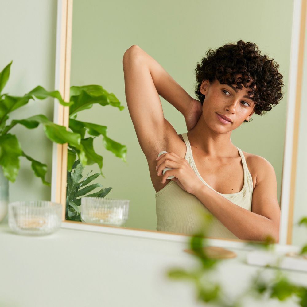 Eine Person benutzt einen Deodorant Roll-on. Spiegelbild zeigt die Person, die den Roll-on unter dem Arm anwendet.