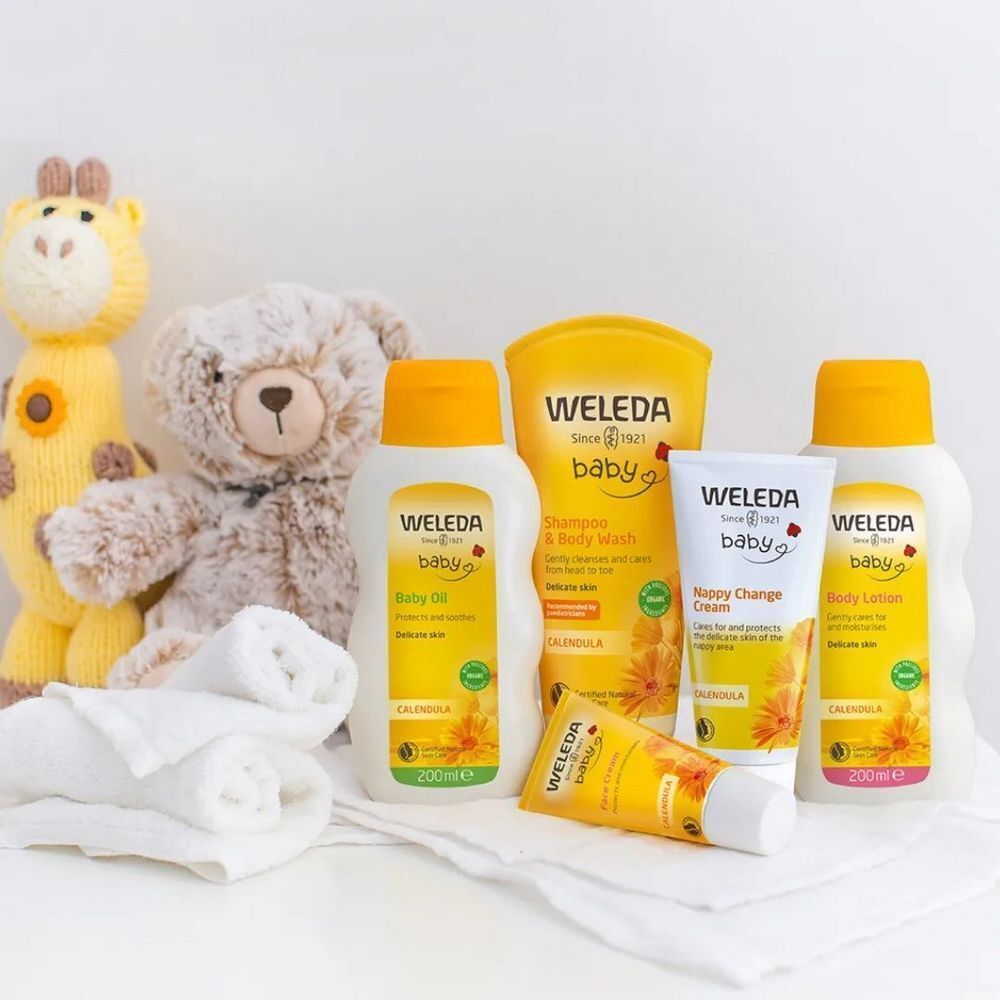 Verschiedene Weleda Baby-Pflegeprodukte. Flaschen, Tuben und Creme mit gelben Etiketten, Produktnamen und Illustrationen. Auf weißem Untergrund.