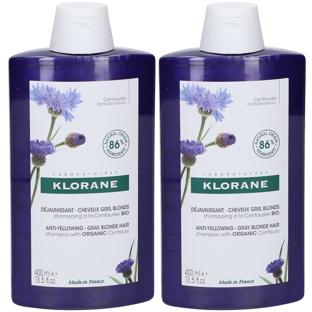 Deux flacons de shampooing Klorane anti-jaunissement. Bouteilles violettes avec bouchons et étiquettes blancs. 86% ingrédients d'origine naturelle.