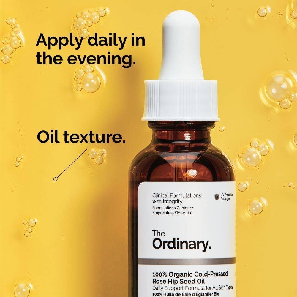 Flacon d'huile de rose musquée 100% biologique The Ordinary avec compte-gouttes sur fond jaune avec des gouttelettes d'huile.