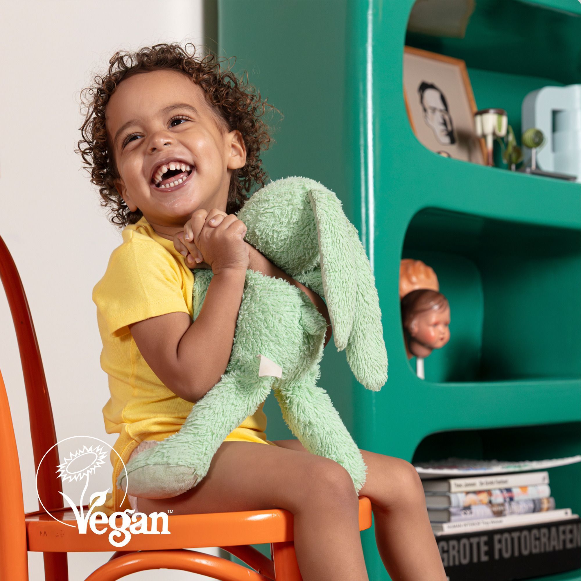 Enfant souriant sur une chaise avec peluche, label Vegan.