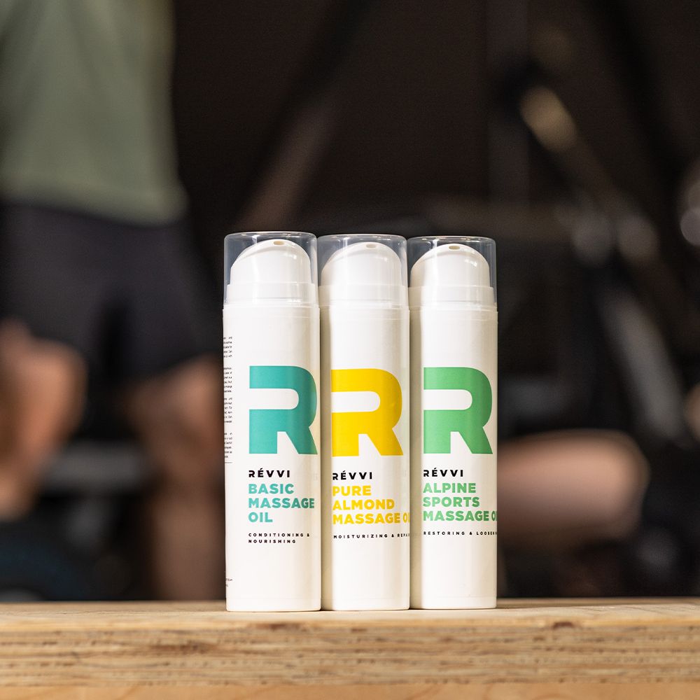 Trois flacons avec pompe. RÉVVI Basic Massage Oil, Pure Almond Massage, Alpine Sports Massage. Sur une surface en bois.
