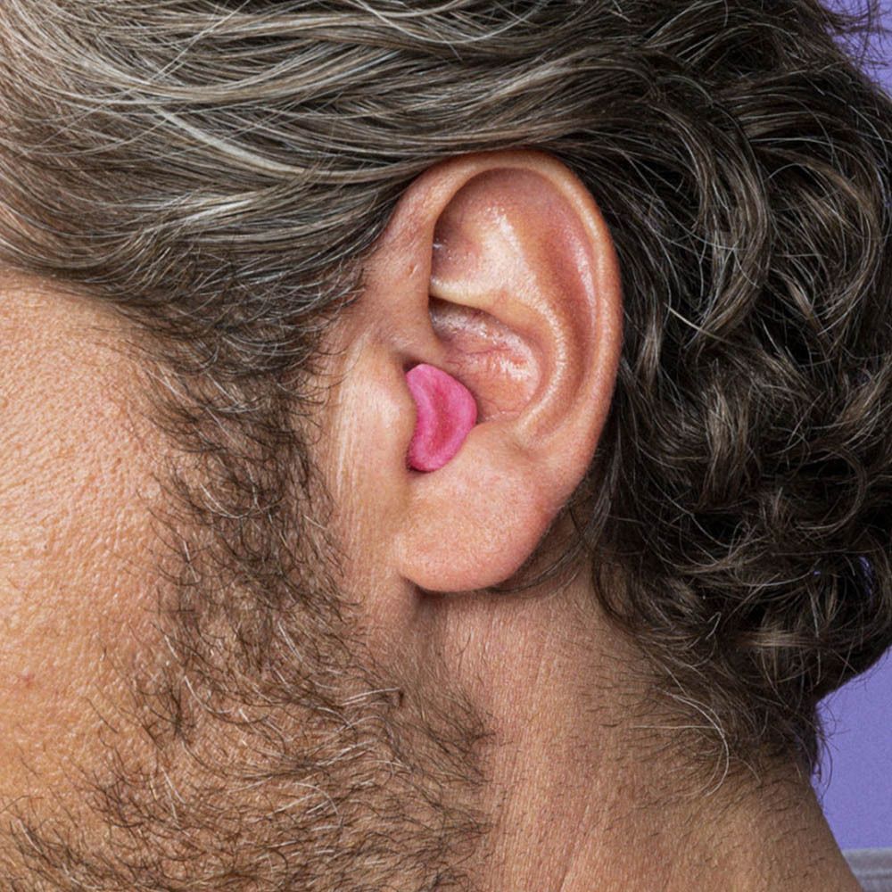 Ein rosa Ohrstöpsel aus Naturwachs, medium, in einem menschlichen Ohr eingesetzt.