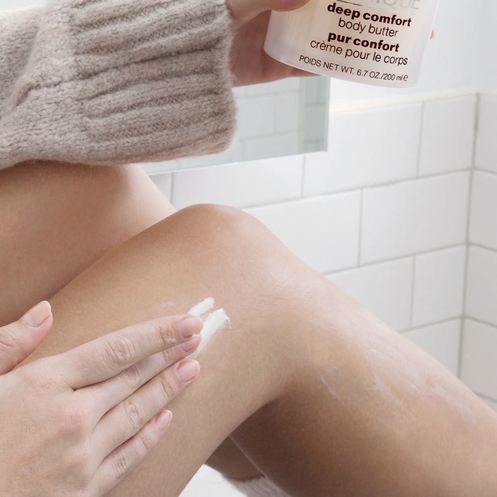 Une main applique le Clinique Deep Comfort Body Butter sur la jambe.