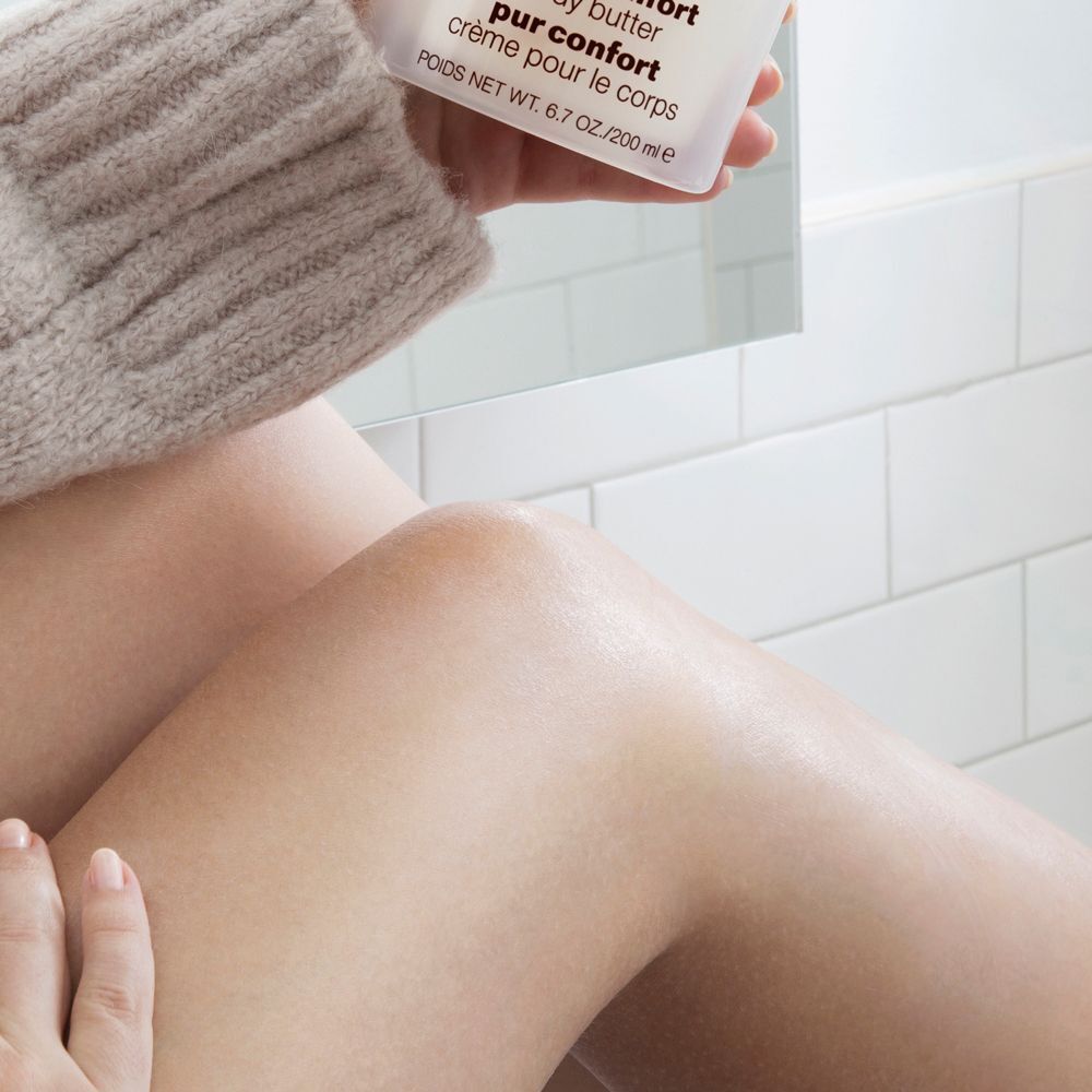 Une personne applique le Clinique Deep Comfort Body Butter sur ses jambes.