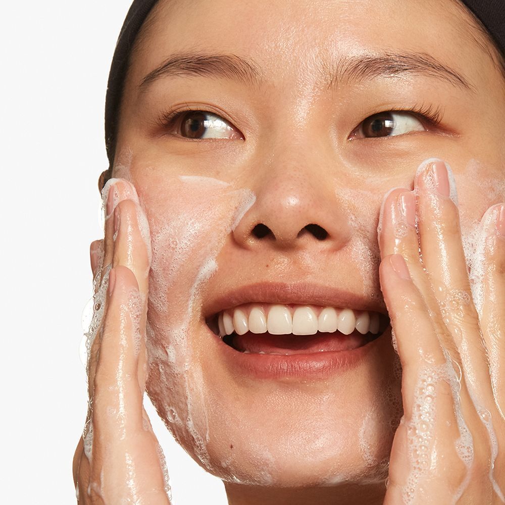 Eine Frau wendet schäumendes Reinigungsgel im Gesicht an.
