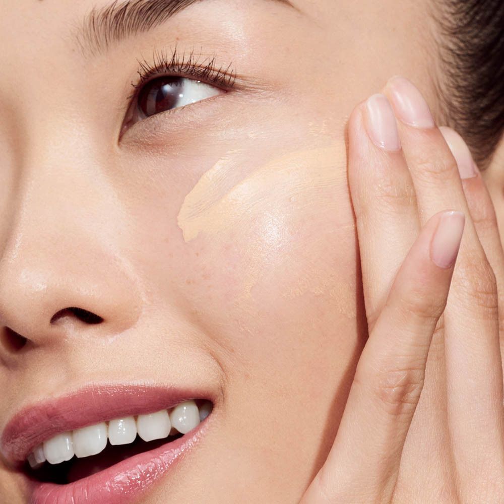 Gros plan d'une femme appliquant Clinique Even Better Vitamin Makeup Light Cool 3 sur sa joue.