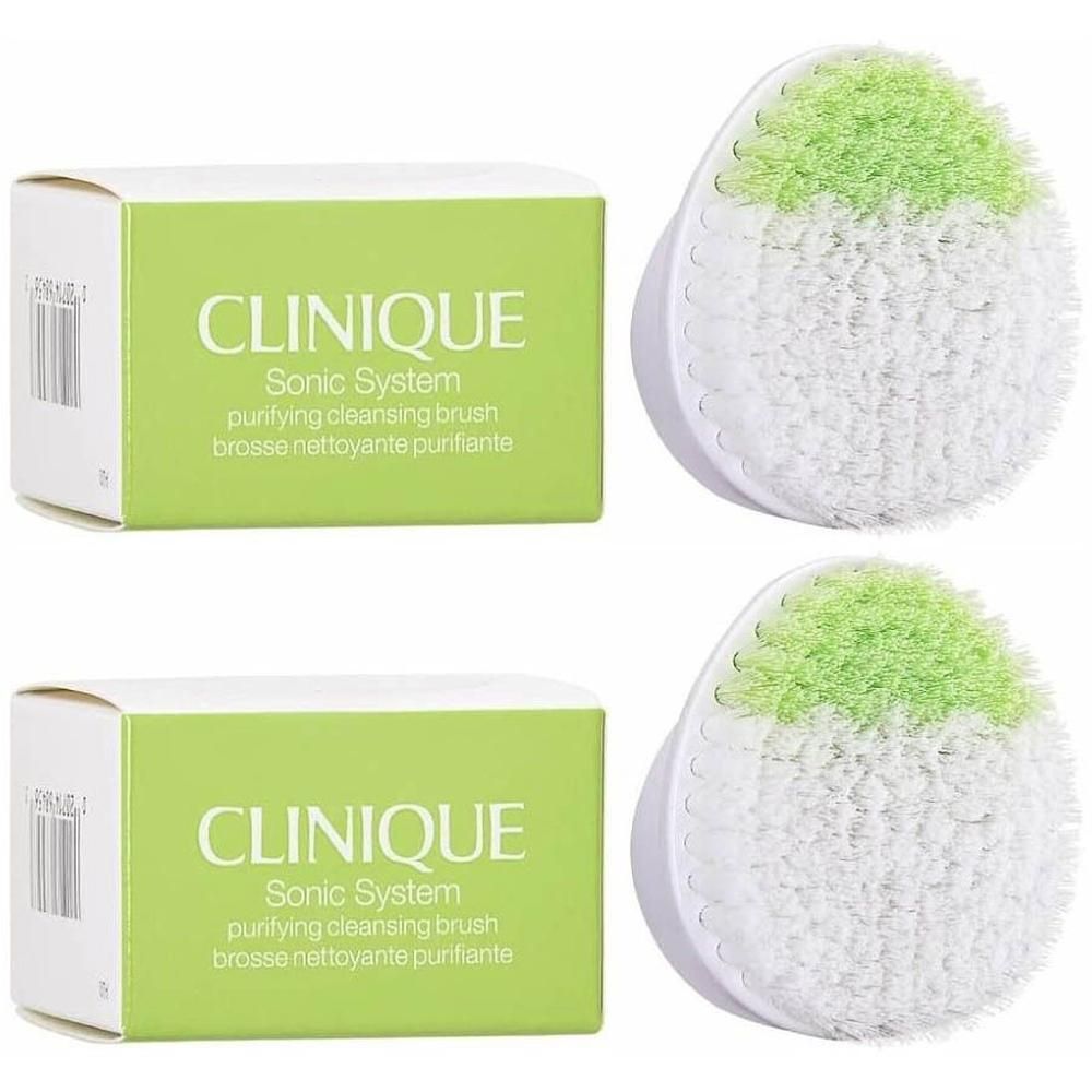 Deux têtes de brosse nettoyante CLINIQUE Sonic System, blanches avec des poils verts, à côté de leurs emballages.