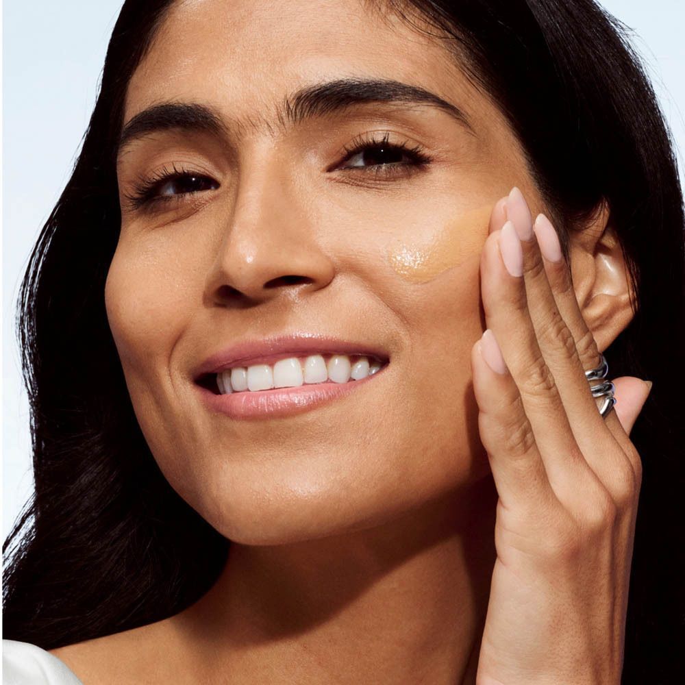 Gros plan d'une femme à la peau foncée appliquant Clinique Even Better Makeup.