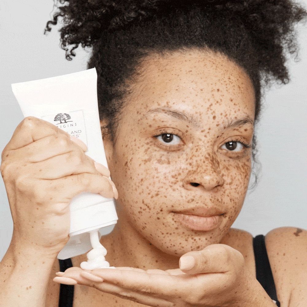 Frau mit Sommersprossen hält eine Tube ORIGINS Checks and Balances™ Frothy Face Wash.