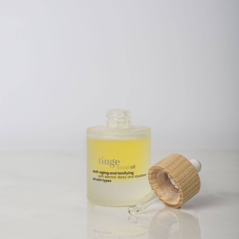 Eine Flasche ting facial Gesichtsöl mit Pipettenverschluss und Holzdeckel, daneben liegend.