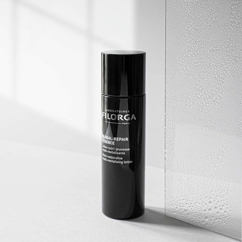 Un flacon noir de FILORGA Global-Repair Essence Lotion à côté d'une surface miroir.