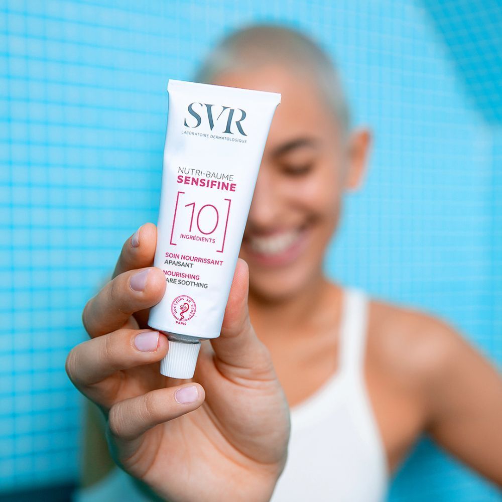 Une main tenant un tube SVR Sensifine Nutri-Baume contenant 10 ingrédients.