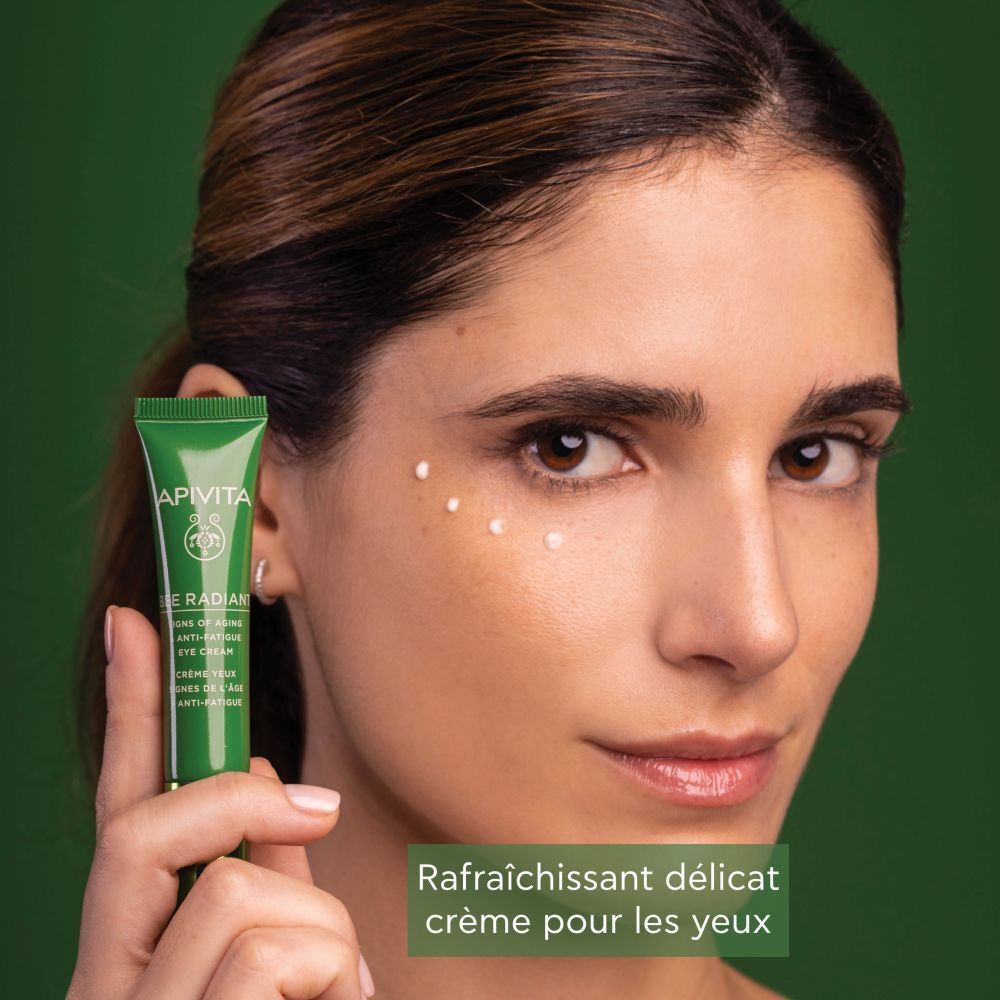 Une femme tient un tube de crème contour des yeux Apivita Bee Radiant, points sur la peau.