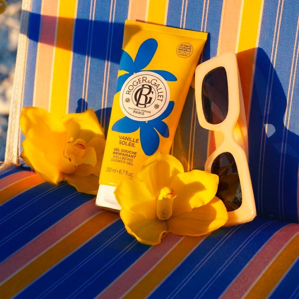 Gelbe Tube Roger&Gallet Vanille Soleil Duschgel, 200 ml, umgeben von Blumen und Vanilleschoten.