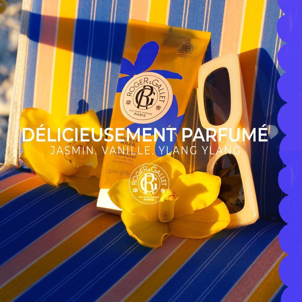 Tube jaune de gel douche Roger&Gallet Vanille Soleil, 200 ml, sur tissu rayé avec lunettes de soleil et fleurs.