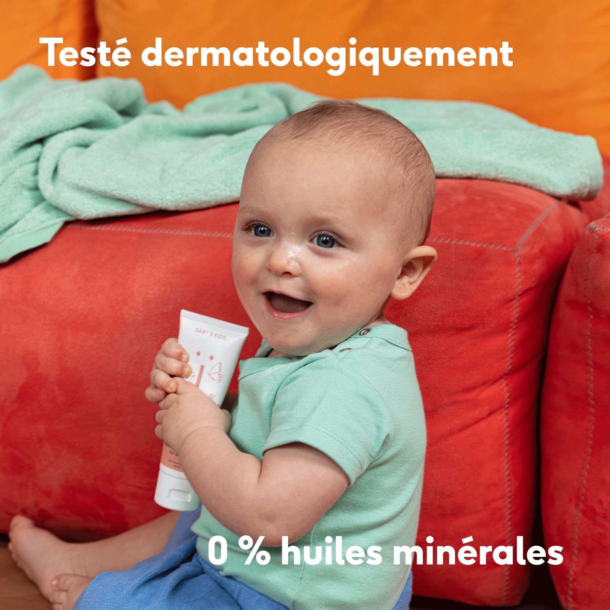 Bébé souriant tenant un tube de crème Naïf, testé dermatologiquement.