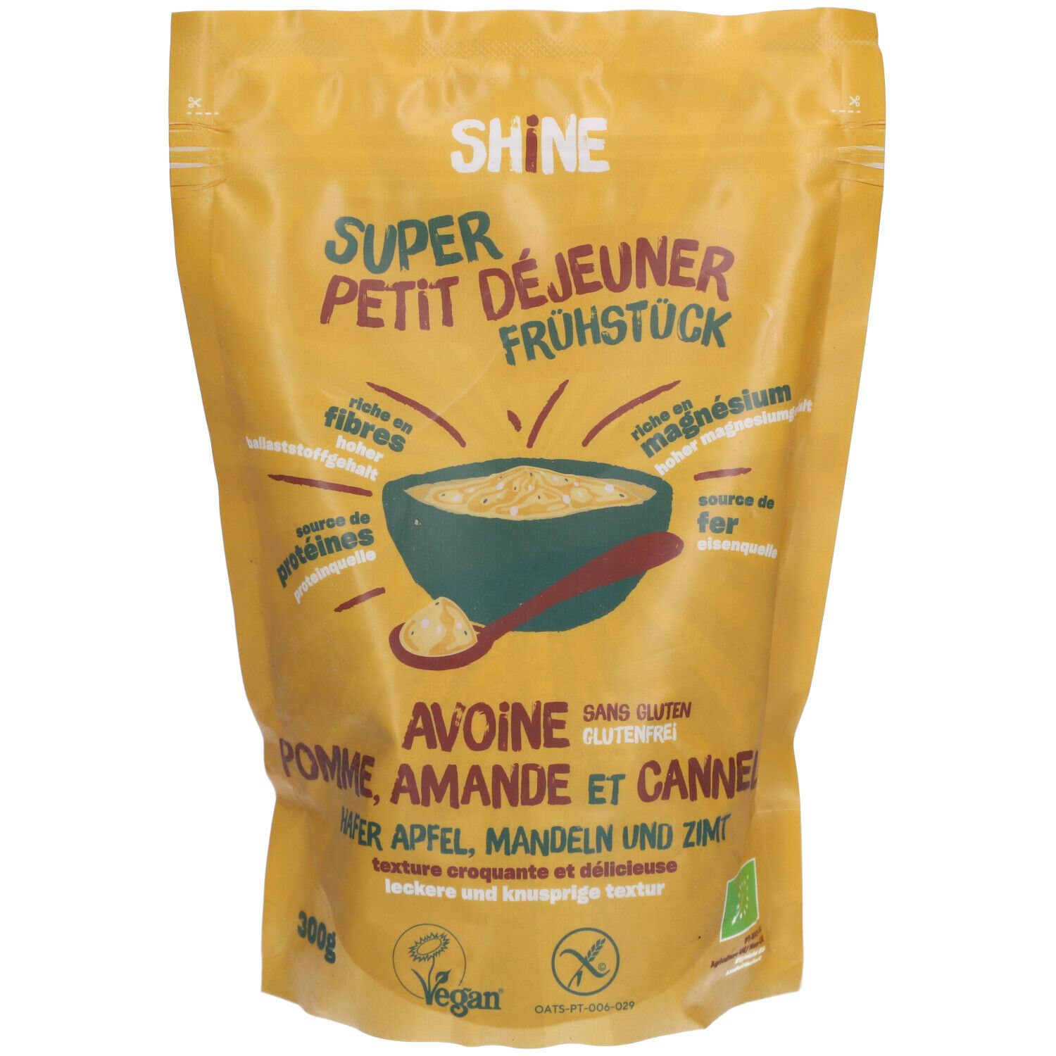 Gelbe Tüte mit Aufschrift "SHINE". Enthält Frühstücksflocken. Text: Hafer, Apfel, Mandel & Zimt. Vegan-Siegel.