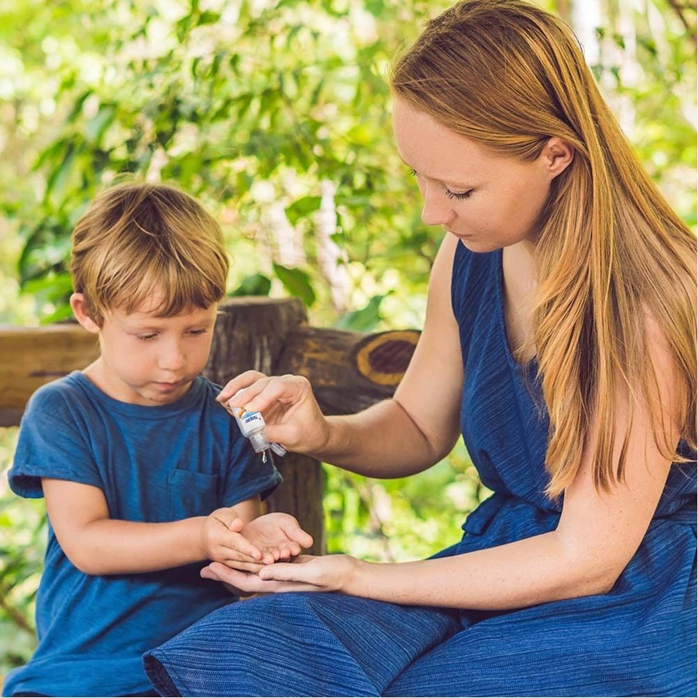 Eine Frau gibt einem Kind Handdesinfektionsmittel auf die Hände. Beide sitzen im Freien.