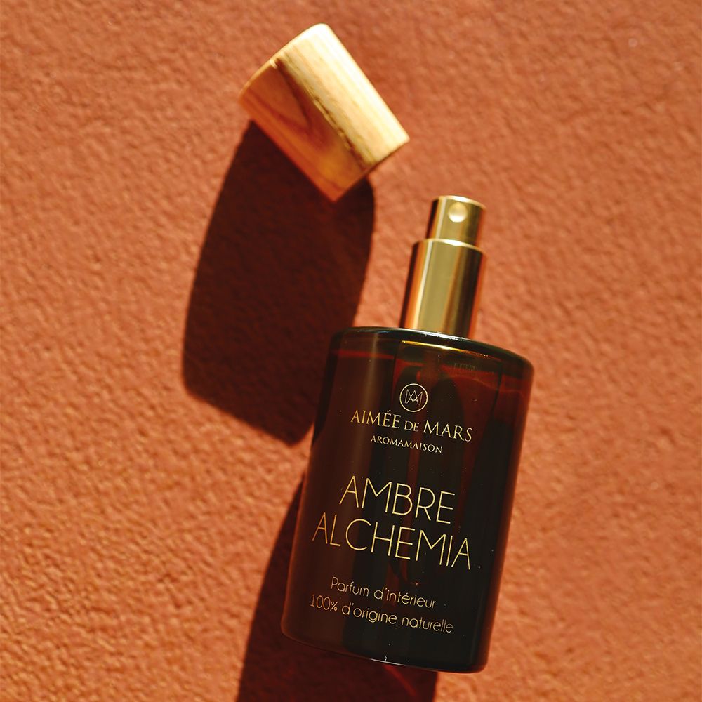 Flacon en verre brun avec bouchon en bois, couvercle à côté. Inscription: AMBRE ALCHEMIA, Parfum d'intérieur, 100% d'origine naturelle.