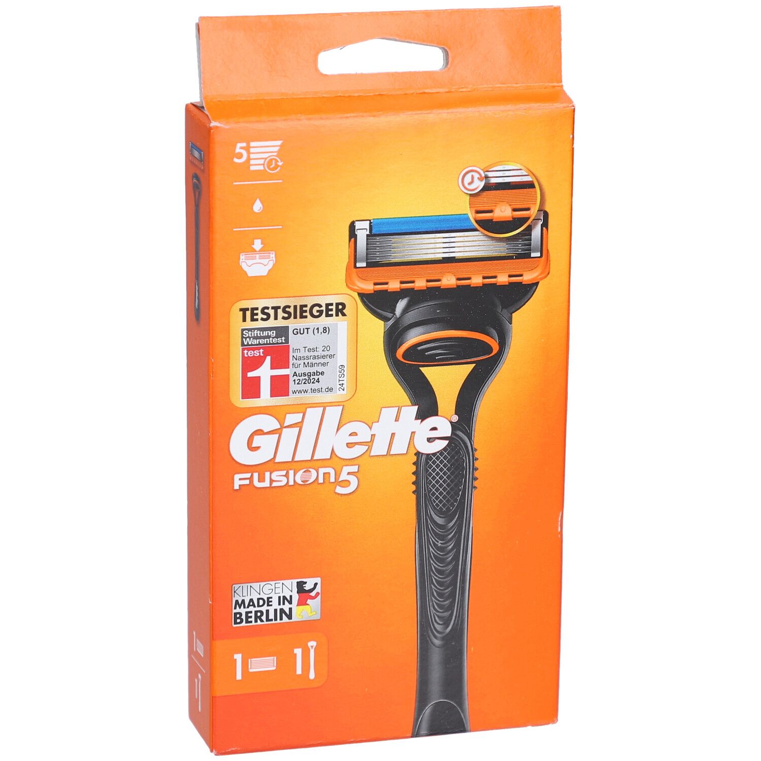 Rasierapparat in orangefarbener Verpackung. Schwarzer Griff, orangefarbener Rasierkopf mit blauer Klinge. Text: Gillette Fusion5, TestSieger.