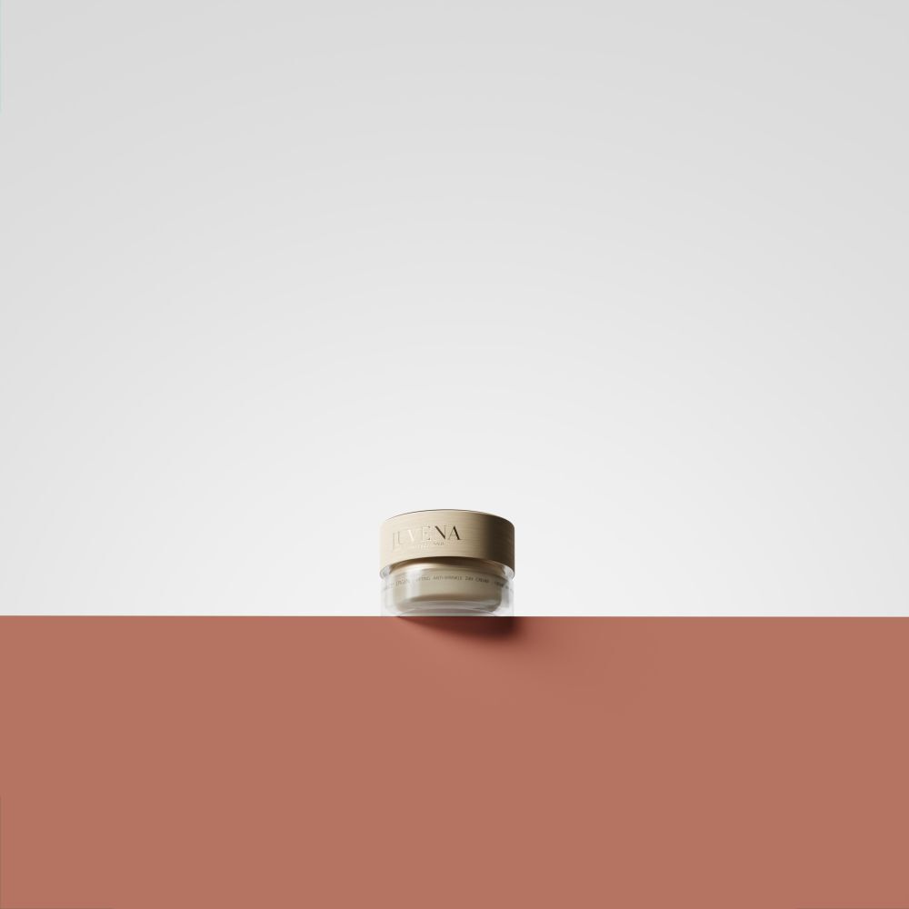 Kleiner Creme-Tiegel mit goldfarbenem Deckel. Aufschrift: Juvena. Auf rotem und weißem Hintergrund platziert.