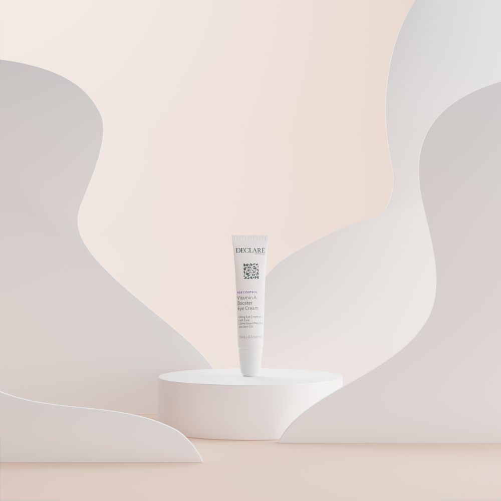Tube DECLARÉ Vitamin A Booster Eye Cream sur socle. Fond: formes abstraites blanches et beiges.