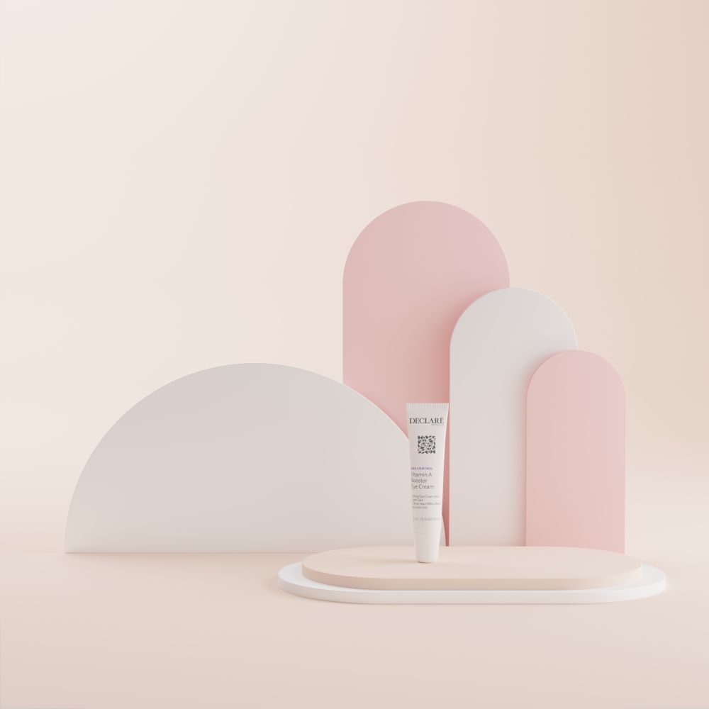 Tube DECLARÉ Vitamin A Booster Eye Cream sur socle. Fond: formes abstraites roses et blanches.