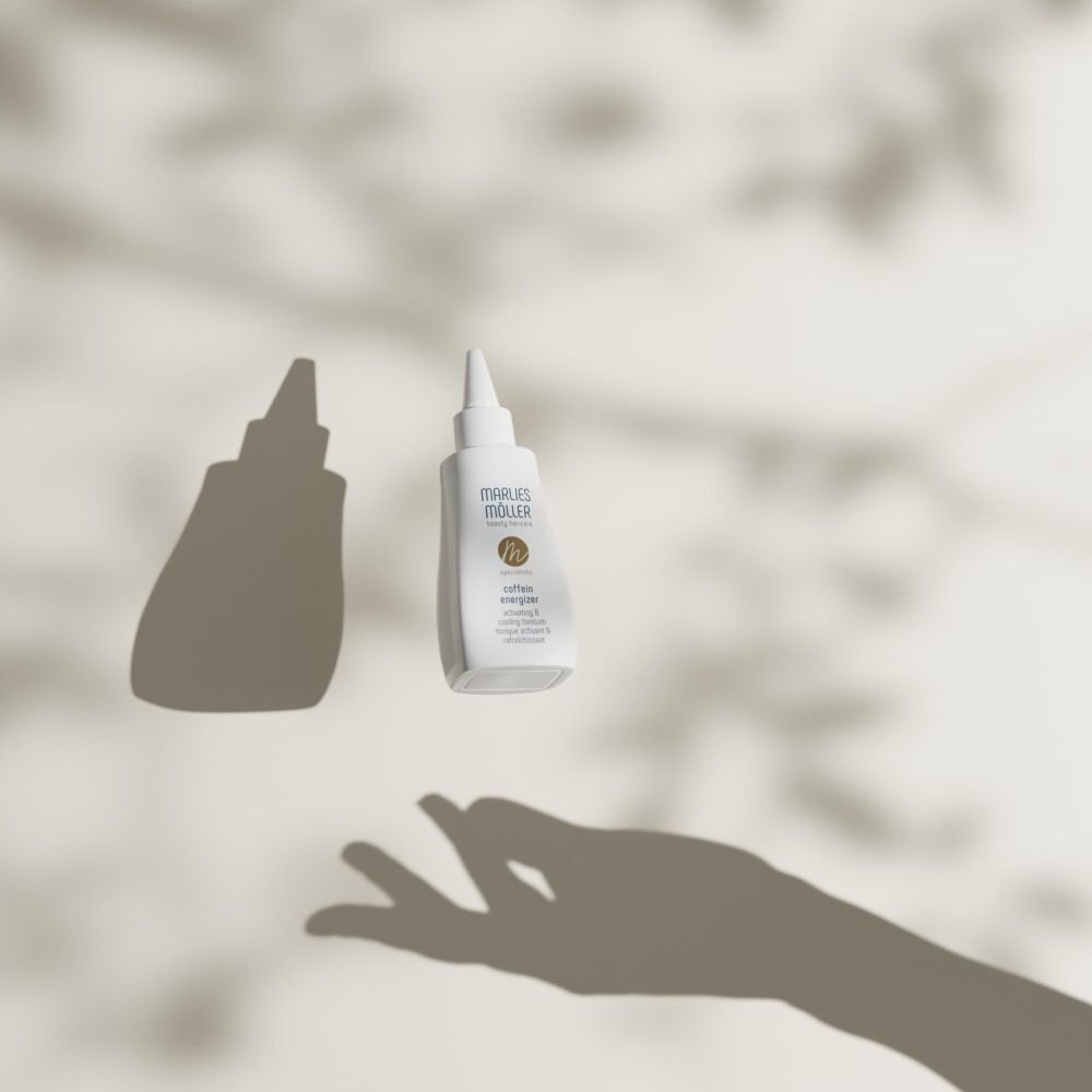 Weiße Flasche mit spitzem Applikator, schwebend. Schatten einer Hand und Blätter.