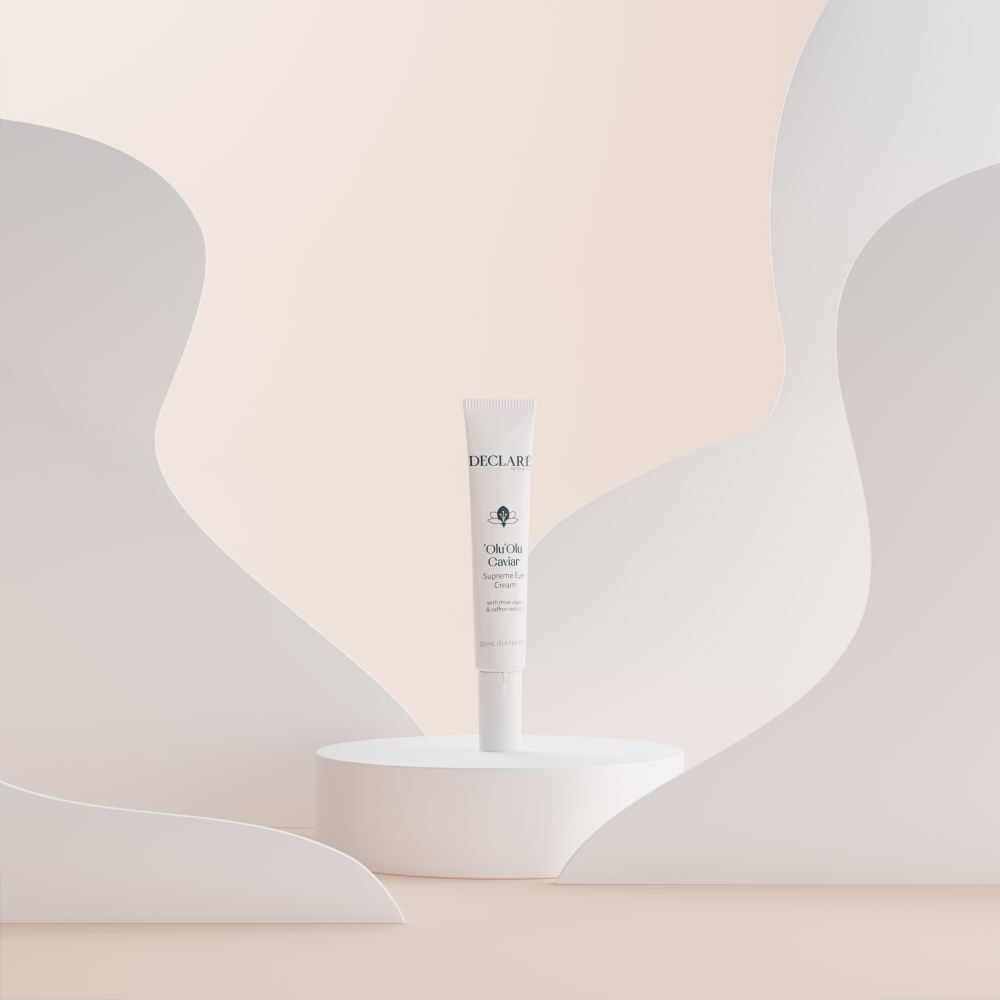 Tube blanc 'Olu'Olu Caviar Supreme Eye Cream sur socle. Fond avec formes blanches. Logo DECLARÉ visible.
