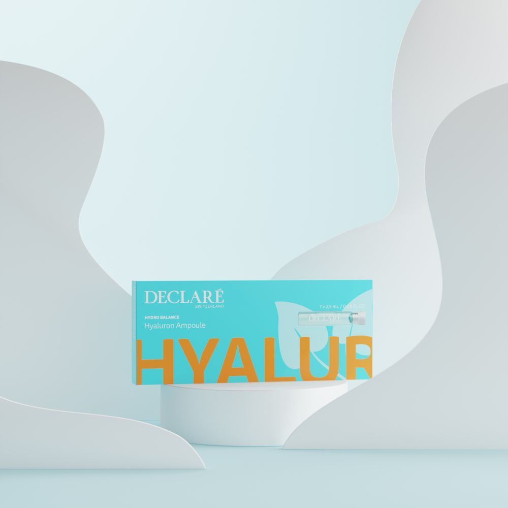 Boîte turquoise avec logo DECLARÉ et nom du produit. Placée sur un piédestal blanc. Fond avec des formes blanches.