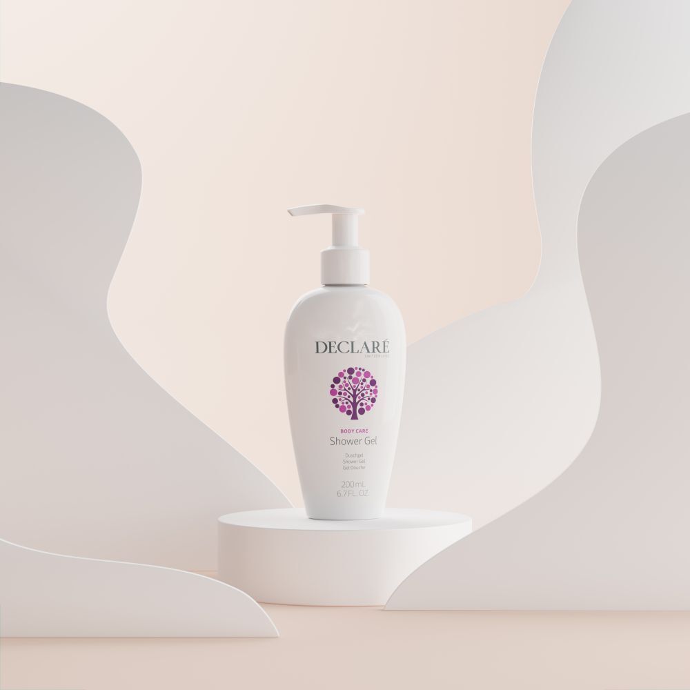 Flacon DECLARÉ blanc avec pompe sur socle. Fond avec formes blanches incurvées. Nom du produit: Shower Gel.