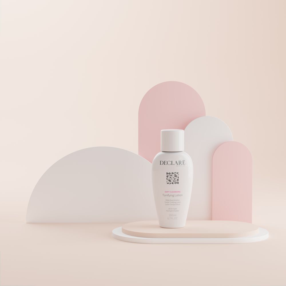 Flacon blanc DECLARÉ Toning Lotion sur socle. Inscription : Soft Cleansing, Toning Lotion. Fond : formes roses.