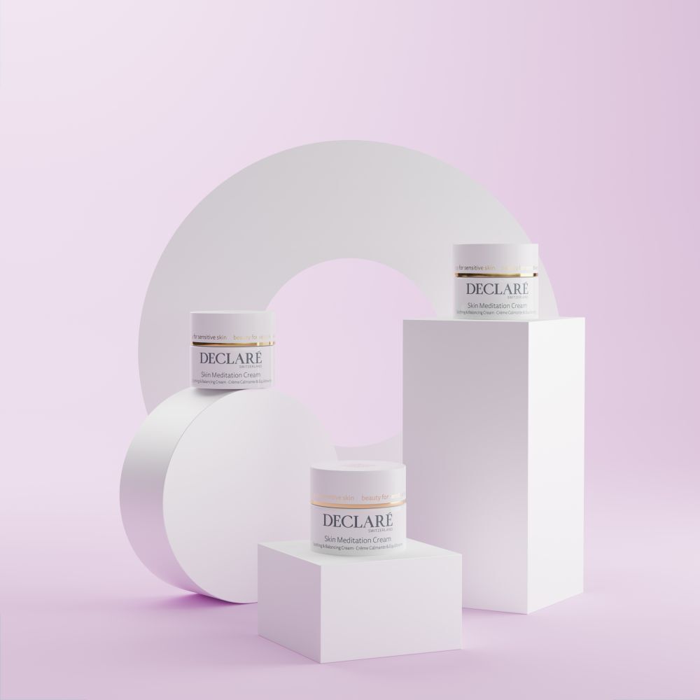 Trois pots de crème sur des socles. Fond avec cercle blanc et éléments roses. Inscription : DECLARÉ Skin Meditation Cream.